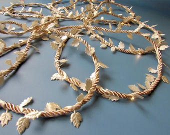 May include: A decorative string of lights featuring a twisted metallic gold rope intertwined with small, die-cut gold leaf accents. The flexible cord is adorned with numerous evenly spaced leaves and integrated warm-toned LED light bulbs.