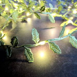 Peut inclure: Une guirlande décorative avec des feuilles vertes en tissu et de petites lumières LED blanc chaud. Les feuilles sont détaillées avec des nervures, et les lumières sont espacées uniformément le long de la vigne. Idéal pour les fêtes ou les événements.
