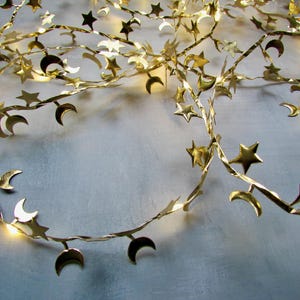 May include: A gold-coloured garland with star and crescent moon decorations. The metal garland is designed for festive use, with evenly spaced stars and moons. Ideal for draping or hanging, it adds a celestial touch to any space.