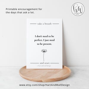 Puede incluir: Una impresión blanca con el texto "No necesito ser perfecto. Solo necesito estar presente". La impresión está sobre una bandeja de madera. La parte superior de la impresión dice "take a breath" y la inferior dice "and reset".