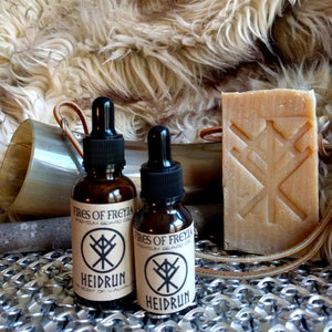 May include: Two small brown glass bottles with droppers, labeled "Fires of Freyja Premium Beard Oil" and "Heidrun The Scent of Valhalla". A bar of soap with a brown label and a symbol is in the background.