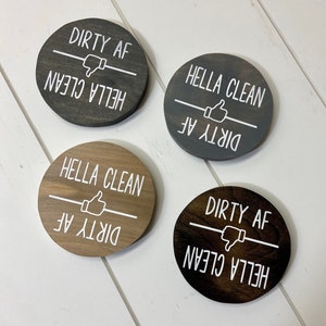 Pode incluir: Quatro placas redondas de madeira com texto branco "DIRTY AF" e "HELLA CLEAN". As placas t&ecirc;m um polegar para cima ou para baixo. As placas s&atilde;o em tons de cinza e castanho.