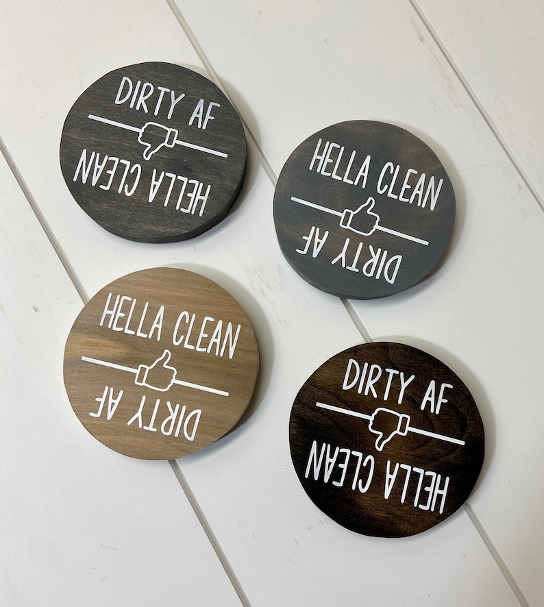 Pode incluir: Quatro placas redondas de madeira com texto branco "DIRTY AF" e "HELLA CLEAN". As placas t&ecirc;m um polegar para cima ou para baixo. As placas s&atilde;o em tons de cinza e castanho.