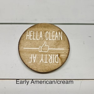 Pode incluir: Uma placa redonda de madeira com as palavras "HELLA CLEAN" acima de um s&iacute;mbolo de polegar para cima e as palavras "DIRTY AF" abaixo. A placa &eacute; marrom clara com letras brancas.