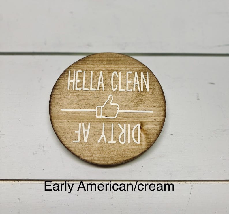 Pode incluir: Uma placa redonda de madeira com as palavras "HELLA CLEAN" acima de um s&iacute;mbolo de polegar para cima e as palavras "DIRTY AF" abaixo. A placa &eacute; marrom clara com letras brancas.