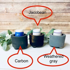 May include: Three wooden k-cup holders in different finishes: carbon, jacobean, and weathered gray. Each holder has a round base with three legs.