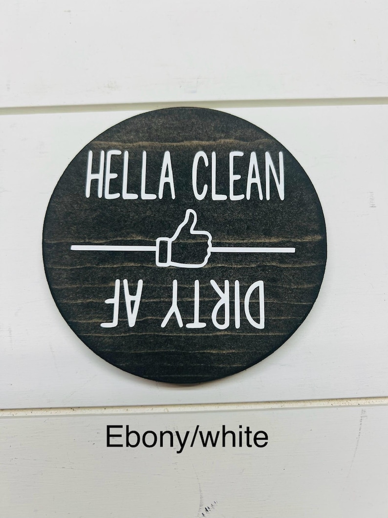 Pode incluir: Uma placa redonda de madeira cor de &eacute;bano com letras brancas. O texto diz "HELLA CLEAN" acima de um s&iacute;mbolo de polegar para cima e uma linha horizontal, com "DIRTY AF" abaixo. A placa &eacute; projetada para cozinha ou decora&ccedil;&atilde;o de casa.