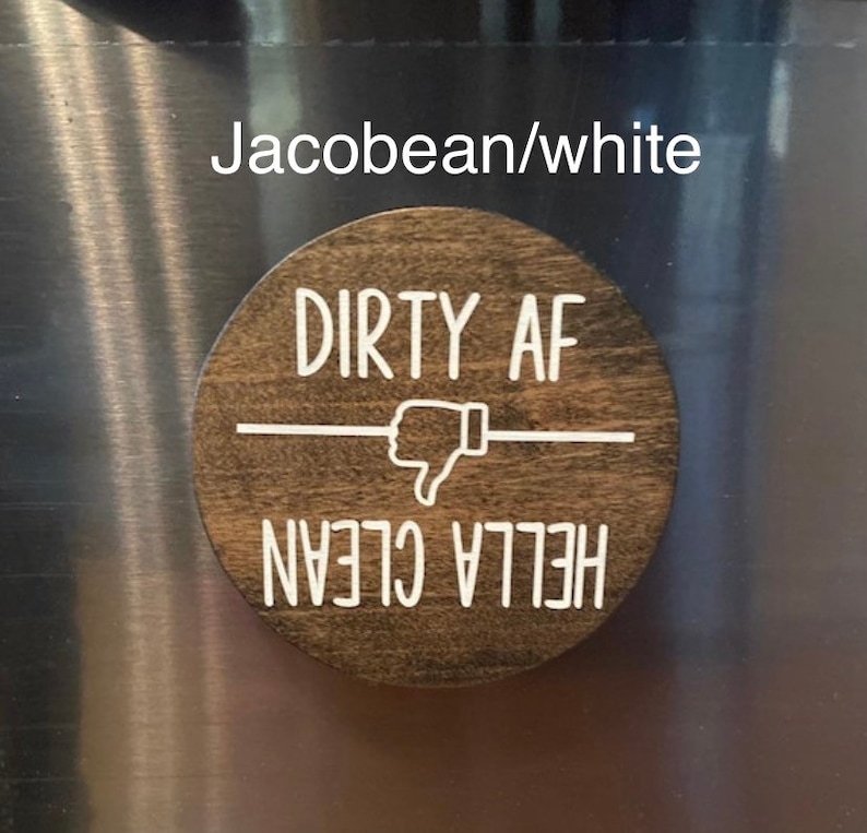 Pode incluir: Uma placa redonda de madeira tingida de castanho escuro com letras brancas. O texto diz "DIRTY AF" acima de um s&iacute;mbolo de polegar para baixo e "HELLA CLEAN" abaixo. Um acess&oacute;rio de cozinha divertido.