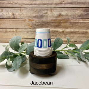 May include: A wooden cup holder with a stack of white paper cups with blue and light blue geometric designs. The holder is dark brown and has a rounded base. The text "Jacobean" is printed below the holder.