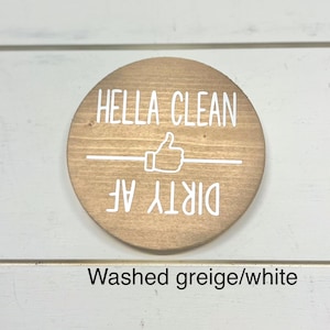 Pode incluir: Uma placa redonda de madeira com as palavras "HELLA CLEAN" acima de um s&iacute;mbolo de polegar para cima e as palavras "DIRTY AF" abaixo. A placa &eacute; marrom claro com letras brancas e uma linha horizontal branca.