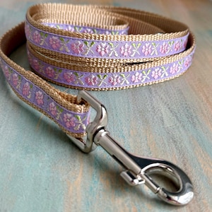 Puede incluir: Una correa de perro beige con un patr&oacute;n floral lavanda y un clip plateado.
