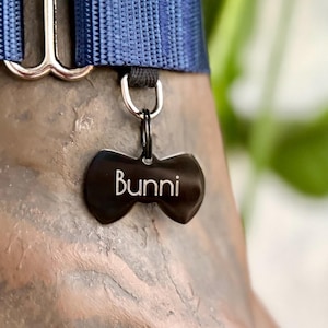 May include: A black bowtie-shaped dog tag with the name "Bunni" engraved in white lettering.