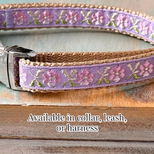 Puede incluir: Un collar de perro marr&oacute;n claro con una cinta morada con un patr&oacute;n floral. La cinta tiene acentos rosados y verdes. El collar est&aacute; disponible en collar, correa o arn&eacute;s.