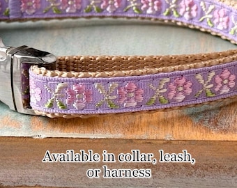 May include: A light brown dog collar with a purple ribbon featuring a floral pattern. The ribbon has pink and green accents. The collar is available in collar, leash, or harness.