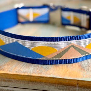 May include: A blue dog collar with a white, yellow, blue, pink, and green geometric mountain and sun design.