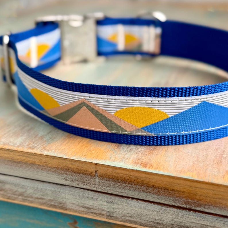 May include: A blue dog collar with a white, yellow, and pink mountain sunset design.