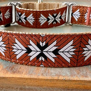 May include: A dog collar featuring a repeating geometric pattern in burnt orange, white, and black. The collar is constructed from durable nylon webbing and includes silver-toned metal hardware, including a sliding adjuster and a D-ring attachment.