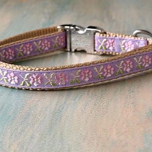 Puede incluir: Un collar para perro de color marr&oacute;n claro con un patr&oacute;n floral morado y rosa. El collar tiene una hebilla plateada y un anillo en D plateado.