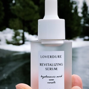 May include: A clear glass bottle with a white dropper top and label. The label reads "LOVERDURE REVITALIZING SERUM hyaluronic acid rose neroli 1 fl. oz."