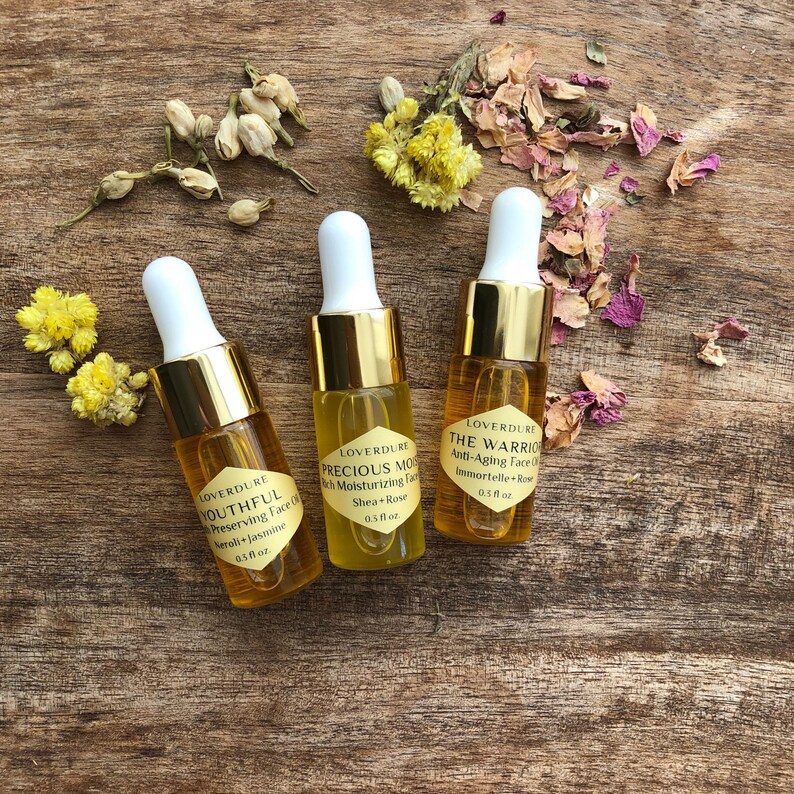 May include: Three small glass bottles with gold caps and droppers filled with face oil. The bottles are labeled with the brand name "LOVERDURE" and the names of the oils: "YOUTHFUL", "PRECIOUS MOS", and "THE WARRIOR".