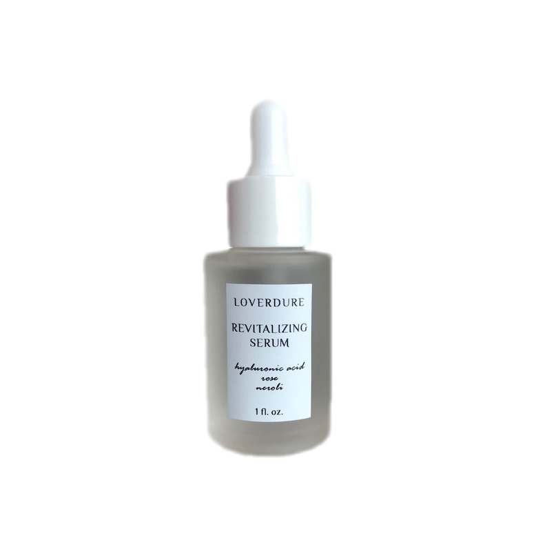 May include: A clear glass bottle with a white dropper top. The bottle is labeled "LOVERDURE REVITALIZING SERUM hyaluronic acid rose neroli 1 fl. oz."