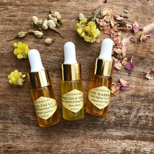 May include: Three small glass bottles with gold caps and labels. The bottles contain face oils with the following names and ingredients: Youthful (Neroli + Jasmine), Precious Moisturizing (Shea + Rose), and The Warrior (Immortelle + Rose). Each bottle is 0.3 fluid ounces.