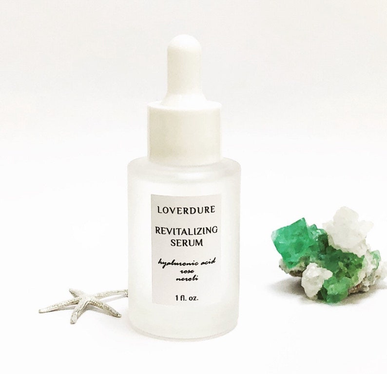 May include: A clear glass bottle with a white dropper top and a white label that reads "LOVERDURE REVITALIZING SERUM hyaluronic acid rose neroli 1 fl. oz."