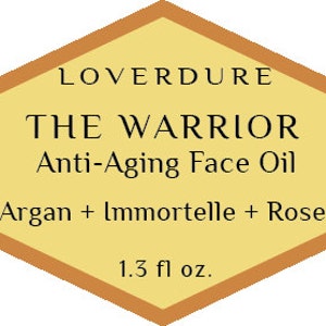 May include: A diamond-shaped label with a gold border and a yellow background. The label reads "LOVERDURE THE WARRIOR Anti-Aging Face Oil Argan + Immortelle + Rose 1.3 fl oz."