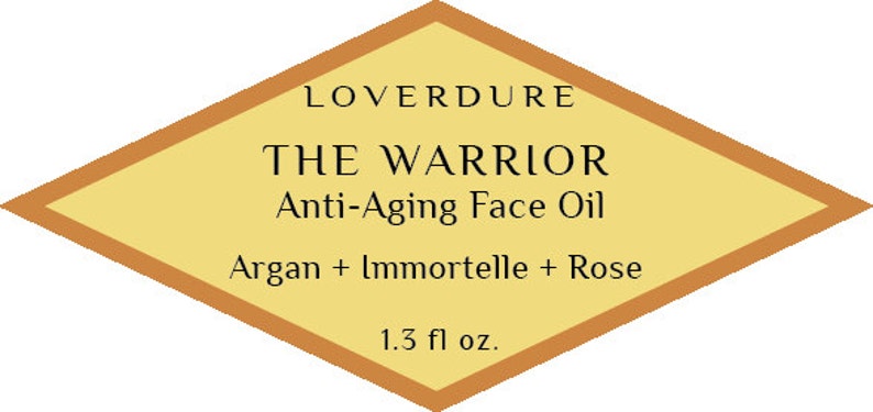 May include: A diamond-shaped label with a gold border and a yellow background. The label reads "LOVERDURE THE WARRIOR Anti-Aging Face Oil Argan + Immortelle + Rose 1.3 fl oz."