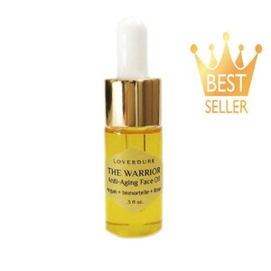 May include: A small, clear glass bottle with a gold cap and dropper. The bottle contains a yellow liquid and is labeled "LOVERDURE THE WARRIOR Anti-Aging Face Oil Argan + Immortelle + Rose .3 fl oz."