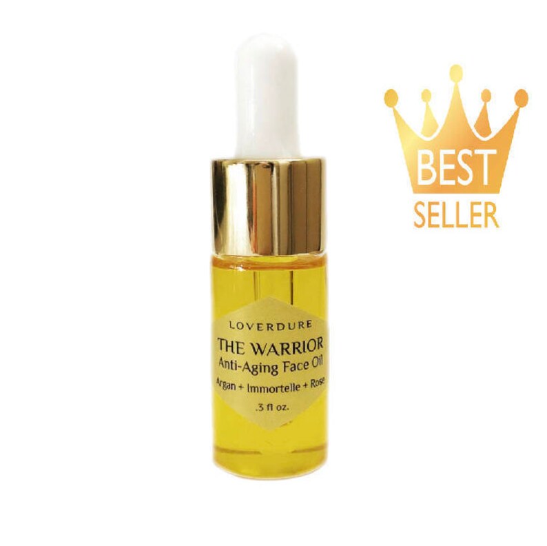 May include: A small, clear glass bottle with a gold cap and dropper. The bottle contains a yellow liquid and is labeled "LOVERDURE THE WARRIOR Anti-Aging Face Oil Argan + Immortelle + Rose .3 fl oz."