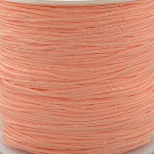 Könnte beinhalten: Eine Spule mit einem pfirsichfarbenen Band, das fest zusammengerollt ist. Das Band ist glatt und scheint aus einem synthetischen Material zu bestehen.