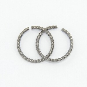 Könnte beinhalten: Zwei silberne, gedrehte Creolen. Die Creolen sind schlicht und elegant.