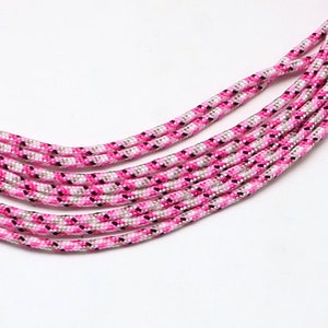 Könnte beinhalten: Rosa, weiß und schwarzes Paracord mit einem geflochtenen Muster.