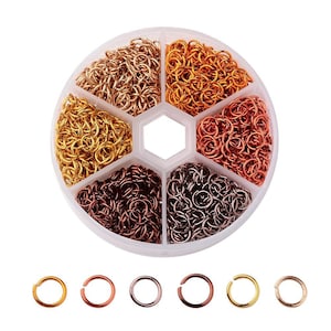 Könnte beinhalten: Ein runder Plastikbehälter mit sechs Fächern, gefüllt mit unterschiedlich farbigen Sprungringen. Die Sprungringe sind in Gold, Kupfer, Roségold und Silber. Unter dem Behälter befinden sich sechs einzelne Sprungringe.