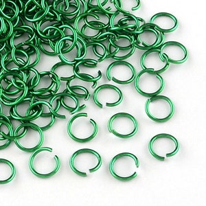 Könnte beinhalten: Haufenweise offene, hellgrüne Sprungringe auf weißem Grund. Die Metallringe haben eine glänzende Oberfläche. Diese Ringe werden häufig in der Schmuckherstellung und bei anderen Bastelprojekten verwendet. Jeder Ring hat einen Durchmesser von ca. 0,8 cm.