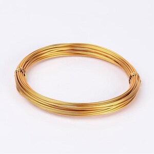 May include: A circular coil of gold-coloured wire. The wire is tightly wound and appears thin and flexible, with a slight sheen. The ends of the coil are secured with a small amount of the same wire. Suitable for jewellery making, the coil is approximately 10 cm in diameter.