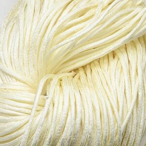 Könnte beinhalten: Nahaufnahme einer Spule mit cremefarbenem Kordel. Der Kordel ist fest gewickelt und hat eine glatte, seidenweiche Textur.