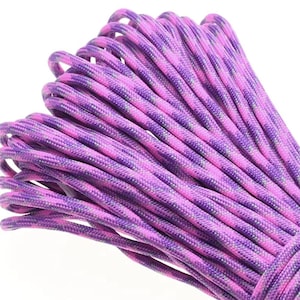 Könnte beinhalten: Ein aufgewickeltes Stück Paracord mit einer gewebten Textur und einem variierenden Muster aus leuchtend violetten, dunkelvioletten und dezenten schwarzen Fäden. Die Schnur ist in parallelen Schlaufen gebündelt und zeigt die komplexe Flechtstruktur.