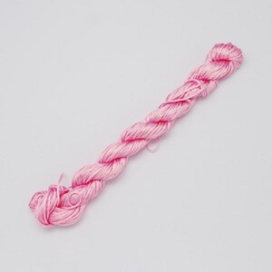 May include: A skein of light pink embroidery floss, tightly wound and twisted. The floss is a soft, pastel pink color, and the strands are smooth and shiny. The skein is neatly bundled, ready for use in various needlework projects.