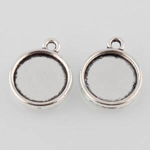 May include: Two silver-toned pendant settings with a round, clear glass insert. The settings have a loop at the top for attaching to a chain or cord.