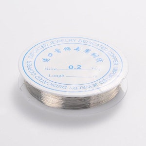 Può includere: Un rotolo di filo color argento per la creazione di gioielli. L'etichetta riporta "IMPORTED JEWELRY DEDICATED COPPER COPPER IMPORTED JEWELRY DEDICATED" in inglese e cinese. L'etichetta indica anche che la dimensione del filo è di 0,2 mm.
