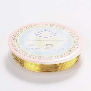 Pode incluir: Um carretel de fio de cobre dourado para fazer joias. O rótulo diz "The Jewelry Appropriation Copper Line" e "Lucky & Lucky". O tamanho é de 2 mm e o comprimento é de 1 metro.