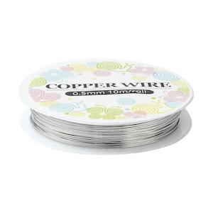 Może przedstawiać: Szpula srebrnego drutu miedzianego z białą etykietą z pastelowymi ilustracjami ślimaków oraz napisem COPPER WIRE 0.5mm 10m/roll. Drut jest ciasno nawinięty wokół środka okrągłej plastikowej szpuli, prezentując metaliczne wykończenie powierzchni.