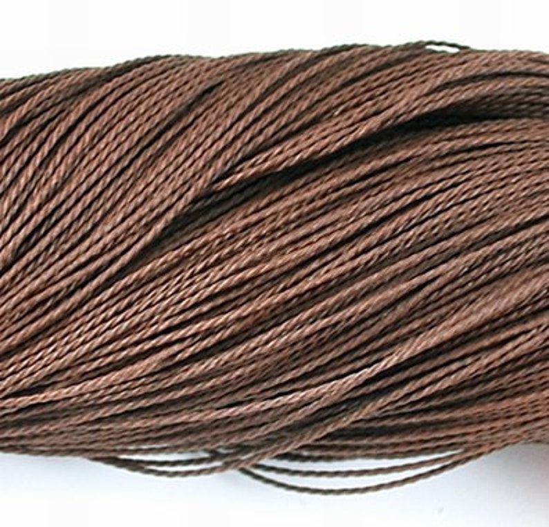 May include: A close-up of a spool of brown waxed cotton cord. The cord is tightly wound and has a smooth, polished finish.