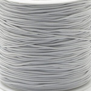 May include: A spool of light grey nylon cord. The cord is tightly wound, showing a textured surface. The colour is a neutral, solid grey, suitable for various crafting projects.