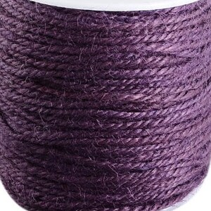 Könnte beinhalten: Eine Spule mit dickem, violettem Jutegarn. Das Garn ist fest gewickelt und hat ein natürliches, rustikales Aussehen.