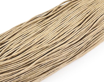 May include: Close-up of a bundle of beige waxed cotton cord. The cords are tightly packed together, creating a textured surface. The color is a neutral tan, suitable for various crafting projects.