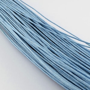 Könnte beinhalten: Ein Bündel aus hellblauem gewachstem Baumwollgarn. Das Garn ist fest zusammengerollt und hat eine glatte, polierte Oberfläche.
