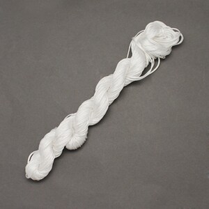 May include: A bundle of white thread, tightly twisted into a rope-like form, lies diagonally across a gray background. The thread appears to be made of a smooth, shiny material, with a slight sheen. The texture suggests it could be used for sewing, crafting, or other textile projects.